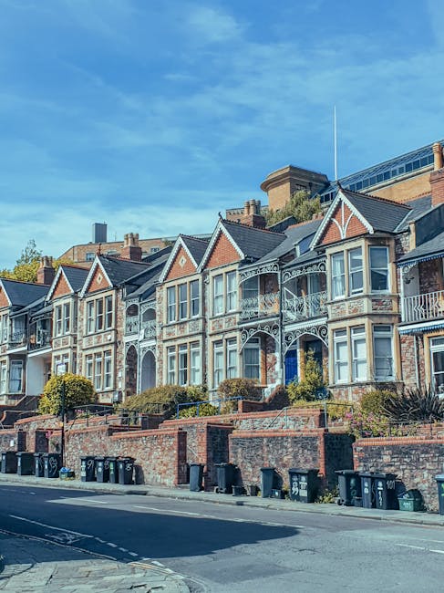 A row of Victorian-style terraced houses located on a residential street, featuring ornate white metalwork balconies and decorative trim on brick facades, with each property having bay windows and sma